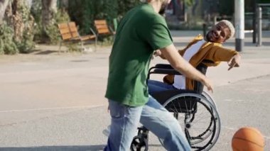 Tekerlekli sandalyedeki neşeli sakat adam eğleniyor, arkadaşlarıyla basketbol oynuyor. 