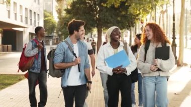 Bir grup üniversite öğrencisi derslerden sonra ellerinde kitaplarla yürüyor, konuşuyor ve gülüyor - Eğitimde kültürel çeşitlilik