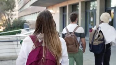 Üniversite binasına doğru yürüyen bir grup arkadaşla birlikte sınıfa giden sarışın öğrenci.