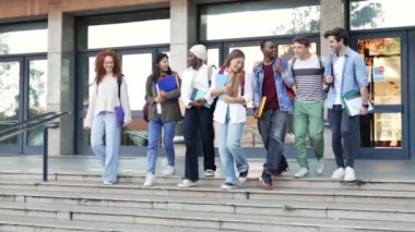 Mutlu öğrenciler üniversite merdivenlerinde birlikte yürüyor, dersten sonra sohbet ediyor ve gülüyorlar.