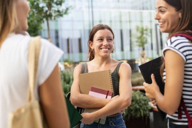 Resmi giyinmiş bir grup genç kadın birlikte duruyorlar, gülümsüyorlar ve el kol hareketi yapıyorlar boş bir etkinlikte hikayelerini paylaşıyorlar. Elleri bellerinde, kalçalarında ve karınlarında eğleniyor gibi görünüyorlar.