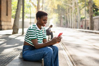 Üniversite kampüsünde sarı kırmızı telefon kullanan mutlu Afrikalı kız. Gülümseyen genç kadın çevrimiçi uygulamayla eğleniyor 