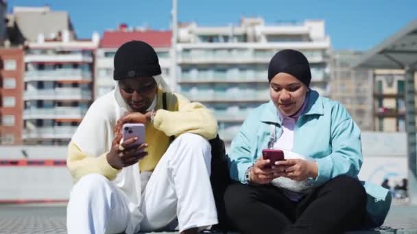Duas Amigas Muçulmanas Sentadas Juntas Usando Telefones Celulares Para Compartilhar Vídeo De Stock Royalty-Free
