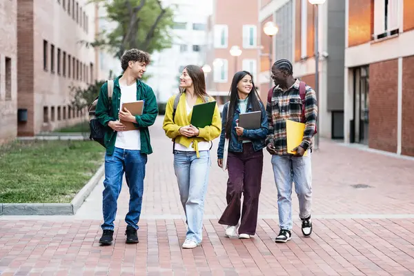 Group of student friends walking on college campus, chatting and laughing after university classes