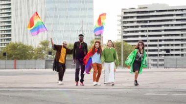 Bir grup insan ellerinde LGBT gökkuşağı bayraklarıyla şehir caddesinde koşuyor.