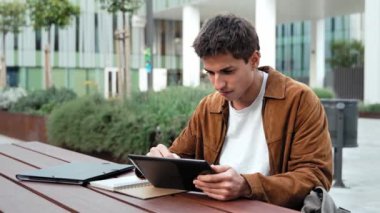 Üniversitede okuyan ve notlar yazan ilham verici bir adam - Öğrenci düşünce ve tabletle çalışıyor