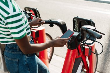 Mobil uygulamalı bir bisiklet kiralama istasyonunda kırmızı bisiklet kiralayan siyahi bir kadın.