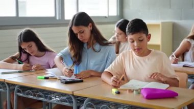 Latin kökenli ilkokul çocuğu ve kız çocukları ilkokuldaki sınıfta egzersiz yazıyorlar. 