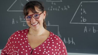 Genç bayan matematik ve geometri öğretmeni ilkokul sınıfında kameraya bakıp gülümsüyor.