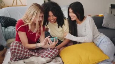 Yatakta cep telefonlarına bakan ve pijama partisinden sonra birlikte gülen genç kız arkadaşlar.