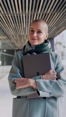 Kurumsal ofis alanında modern bir iş kadını yürüyor. Güçlü, kısa saçlı, kameraya bakan bir kadın.