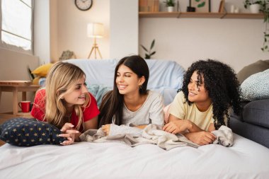 Genç bayan arkadaşlar mutlu bir şekilde sohbet ediyor ve yatakta hikayelerini paylaşıyorlar.