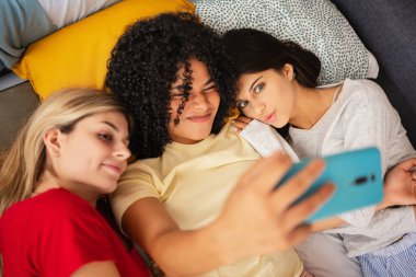 Genç bayan arkadaşlar yatakta eğlenceli bir selfie çekmek için aptalca suratlar yapıyorlar.
