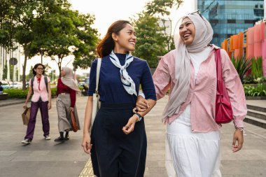 Tesettürlü Asyalı kadınlar ve açık havada eğlenmek - Mutlu Endonezyalı bayan arkadaşlar alışveriş yaparken geziniyor ve konuşuyorlar