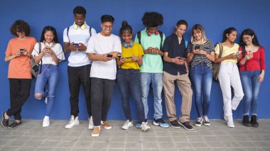 Mavi duvara yaslanmış cep telefonu kullanan bir grup öğrenci.