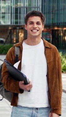 Üniversite kampüsünde kameraya bakarak mutlu bir şekilde duran gülümseyen öğrenci