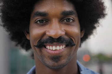 Bıyıklı ve saçlı, gülümseyen neşeli, Afro-Amerikan bir adamın yakın plan portresi.
