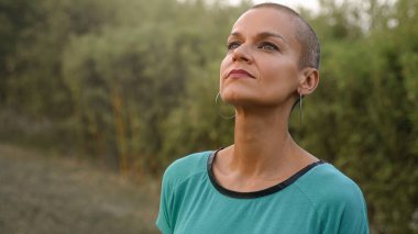 Kafası tıraşlı rahat bir kadın, temiz hava soluyor, doğada meditasyon yapıyor, barışın tadını çıkarıyor. Ruhani Umut