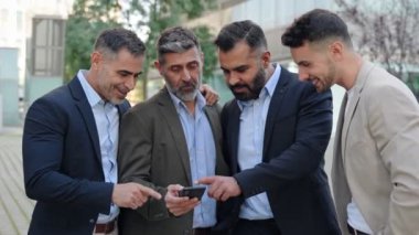 İşten sonra cep telefonu uygulamasına bakan bir grup neşeli iş adamı eğlenceyi paylaşıyor.