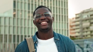 Üniversite kampüsünde gülümseyen gözlüklü ve kot gömlekli neşeli Afrikalı Amerikalı öğrenci