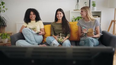 Çeşitli mutlu ev arkadaşları evde TV izlerken sağlıklı yemek yiyor ve dışarıdan yemek yiyorlar.