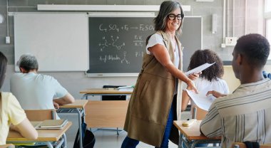 Bayan öğretmen lise öğrencilerine sınav kağıdı veriyor. Üniversite için Yüksek Öğrenim Hazırlığı