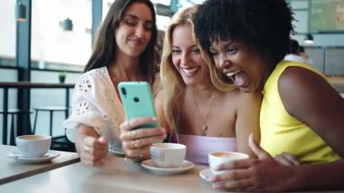 Üç neşeli bayan Gil arkadaşı bir cep telefonu uygulamasına bakıyor ve kafede otururken gülüyorlar.