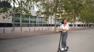 Şehirde elektrikli scooter kullanan genç bir İspanyol kadın.