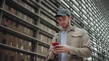 Modern şehir şehrinde cep telefonu kullanan genç bir adam. Kampüste gülümseyen mutlu üniversite öğrencisi