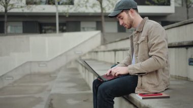 Üniversite öğrencisi dizüstü bilgisayarla çalışıyor. Üniversite merdivenlerinde oturuyor.