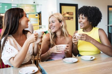 Bir grup bayan arkadaş birlikte kafeteryada konuşuyor ve gülümsüyor, kahvenin tadını çıkarıyorlar.