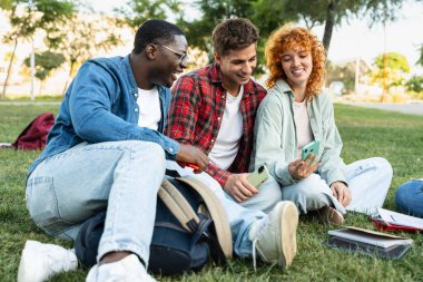 Dışarıda oturan üç farklı öğrenci cep telefonlarına bakıp birlikte komik videolara gülüyorlar.