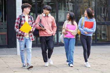 Bir grup üniversite öğrencisi dersten sonra yürüyor ve sınavlarda kitap tutuyor ve gülüyor.