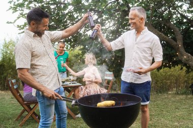 İki olgun erkek arkadaş bahçede barbekü partisinde bira şişeleriyle kadeh kaldırıyor.