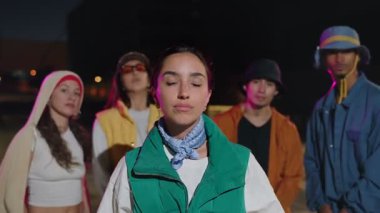 Modern funky tarzı modaya uygun bir arkadaş grubuyla İspanyol bir kadın gece şehirde kameraya bakıyor.