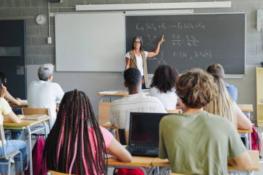 Fen öğretmeni lise öğrencilerine kimya formüllerini ve matematik denklemlerini açıklıyor.
