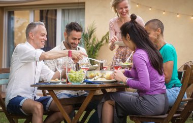 Bir grup yetişkin arkadaş birlikte dışarıda yemek yiyor, yemek yiyor, içki içiyor ve evde eğleniyorlar.
