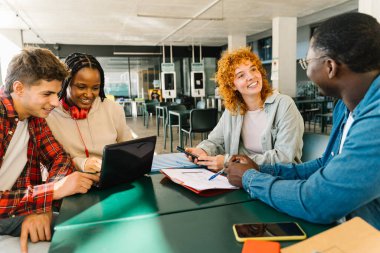 Üniversite kütüphanesinde kitaplarla ve dizüstü bilgisayarla sınavlara çalışan mutlu üniversite öğrencileri.