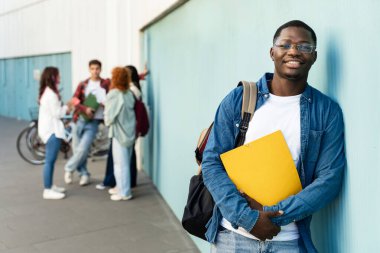 Kampüste durmuş kameraya bakıp gülümseyen genç bir Afro-Amerikan üniversite öğrencisi. 