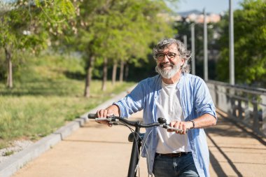 Yaşlı adam Urban Park 'ta bisikleti iterek yürüyor. Sağlıklı ve aktif, rahatlatıcı yaşam tarzı 