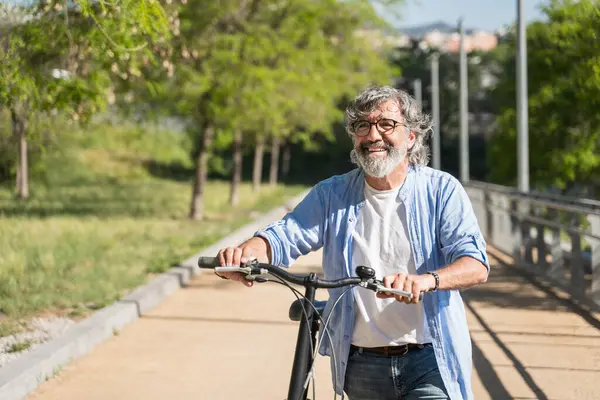 Yaşlı adam Urban Park 'ta bisikleti iterek yürüyor. Sağlıklı ve aktif, rahatlatıcı yaşam tarzı 