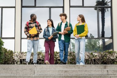 Çeşitli öğrenciler üniversite merdivenlerinden çıkıp konferanslar ve sınavlardan sonra konuşuyor ve gülüyor.
