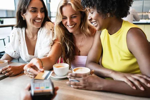 Kafeteryada oturup para ödeyen bir grup mutlu kız arkadaş.