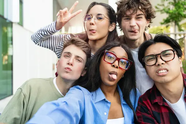 Genç öğrenci arkadaşlar dalga geçiyor ve komik suratlar yapıyor. Gençler arası arkadaşlık selfie çekiyor. Birlikte eğleniyorlar. 