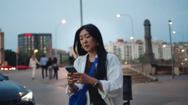 Gece şehirde yürüyen Asyalı bir kadın cep telefonuyla karşıdan karşıya geçerken arkadaşıyla buluşacak.