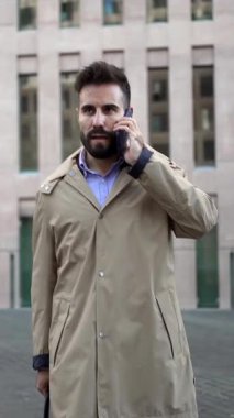 Ciddi bir işadamı, profesyonel evrak çantası taşıyan bir telefonla sokakta yürüyor.