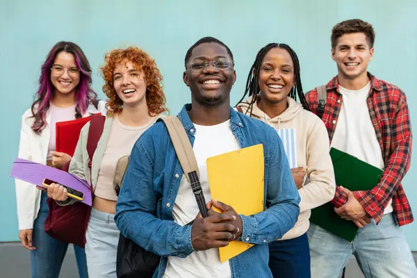 Afrikalı Amerikalı öğrenci ve üniversite sınıf arkadaşı. Mavi duvarda duran gülümseyen öğrenciler