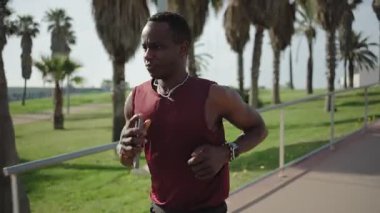Genç Afrikalı Amerikalı bir adam sahilin yakınındaki bir parkta koşuyor, sabah sporunun keyfini çıkarıyor.