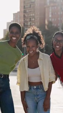 Üç neşeli Afro-Amerikalı kadın bir şehir şehrinde birlikte durup gülümsüyor. Kız Portresi