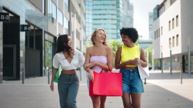 Çok ırklı kız arkadaşlar şehirde yürüyor, birlikte eğleniyor ve hafta sonu alışverişte konuşuyorlar.